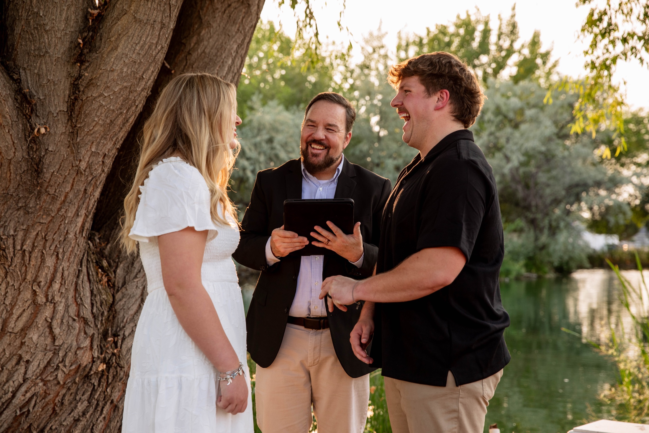 Couple laughing with their officiant at a lakeside ceremony