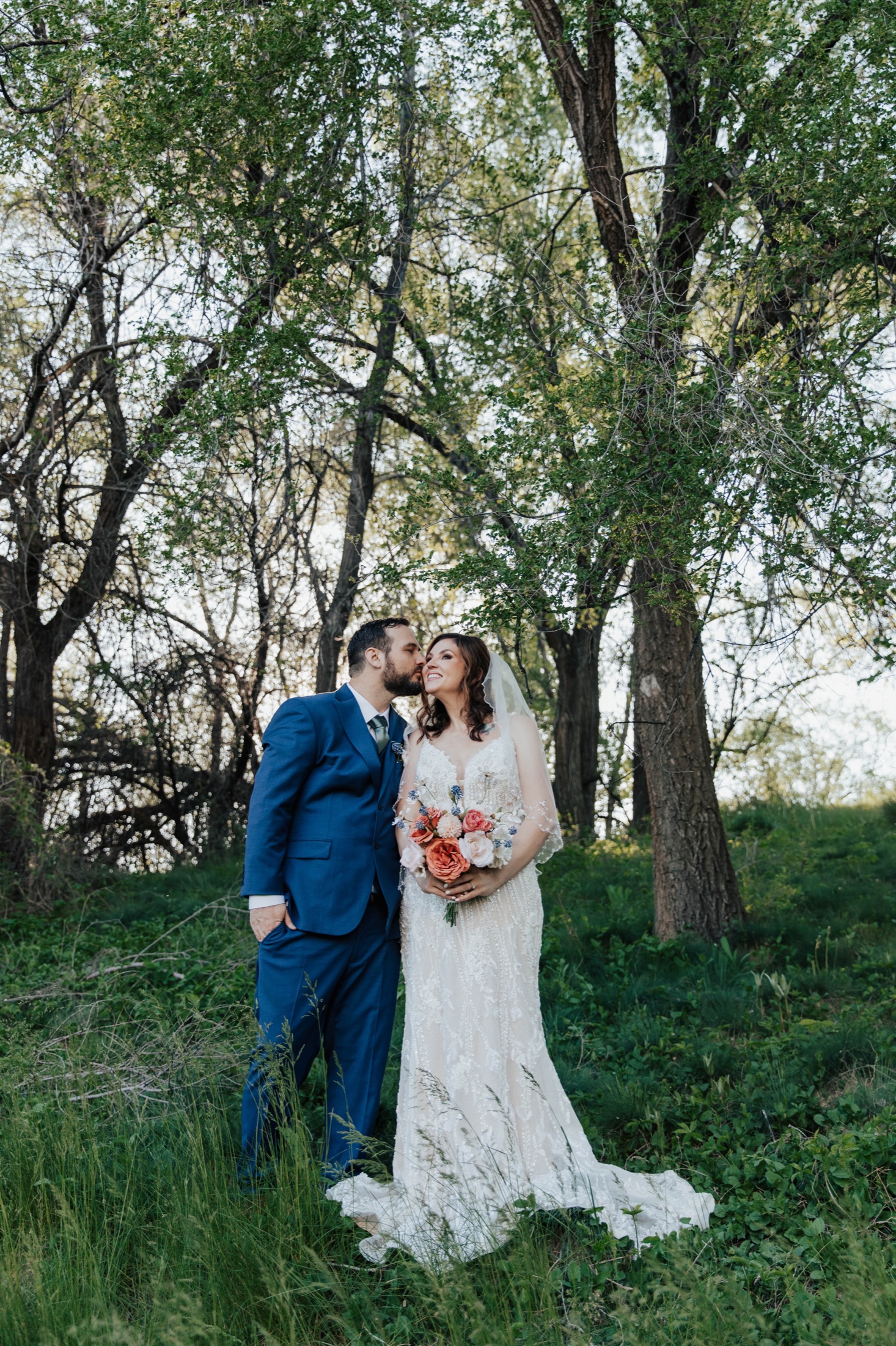 Couple kissing among the trees, bouquet in hand