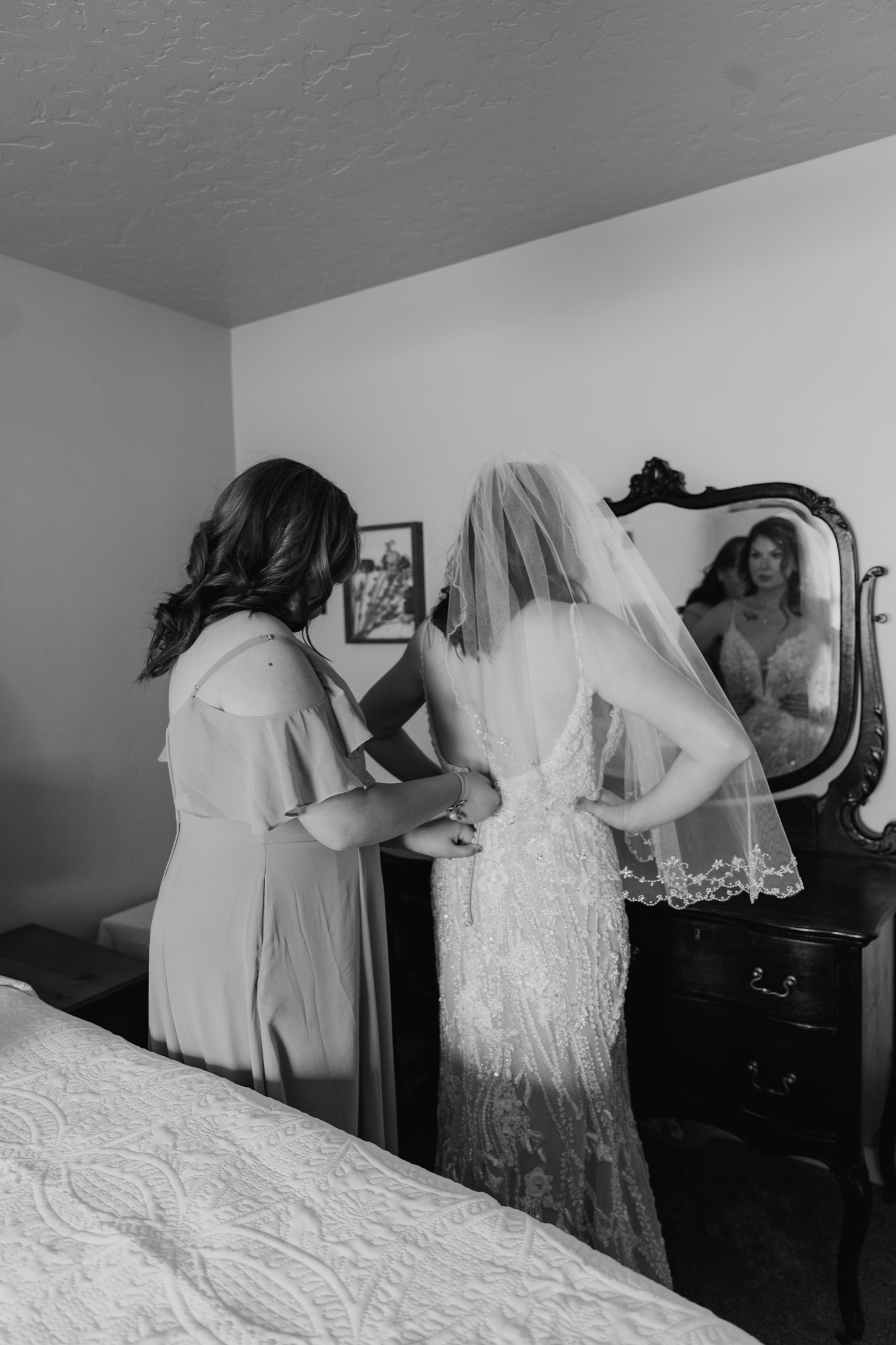 Bridesmaid buttoning the wedding gown in the mirror